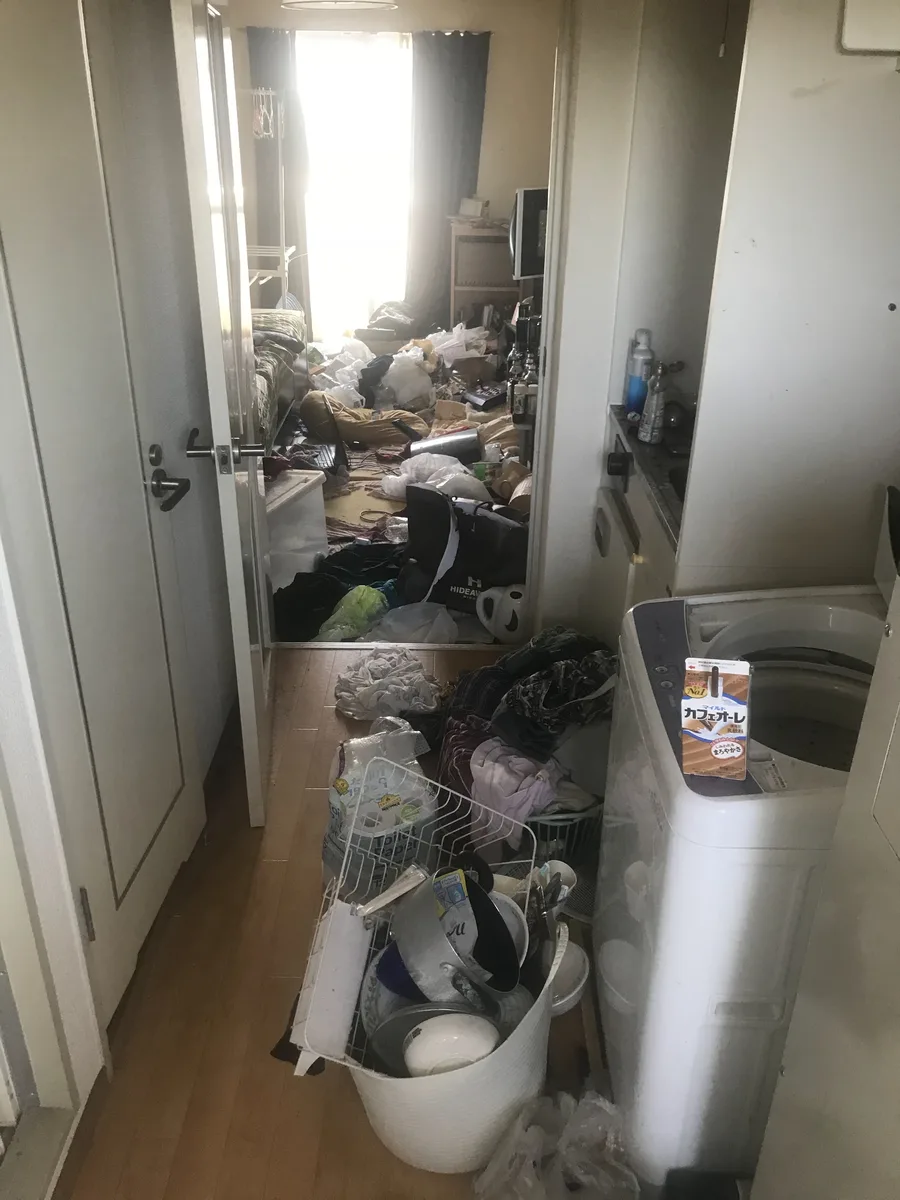ゴミ屋敷清掃前の1Kアパート廊下 — 不用品が溢れた状態